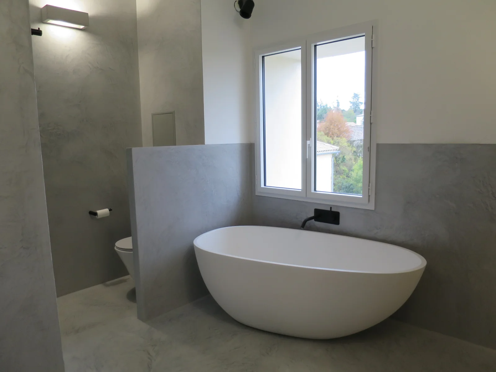 Baignoire devant la fenêtre et matières grises de la salle de bain